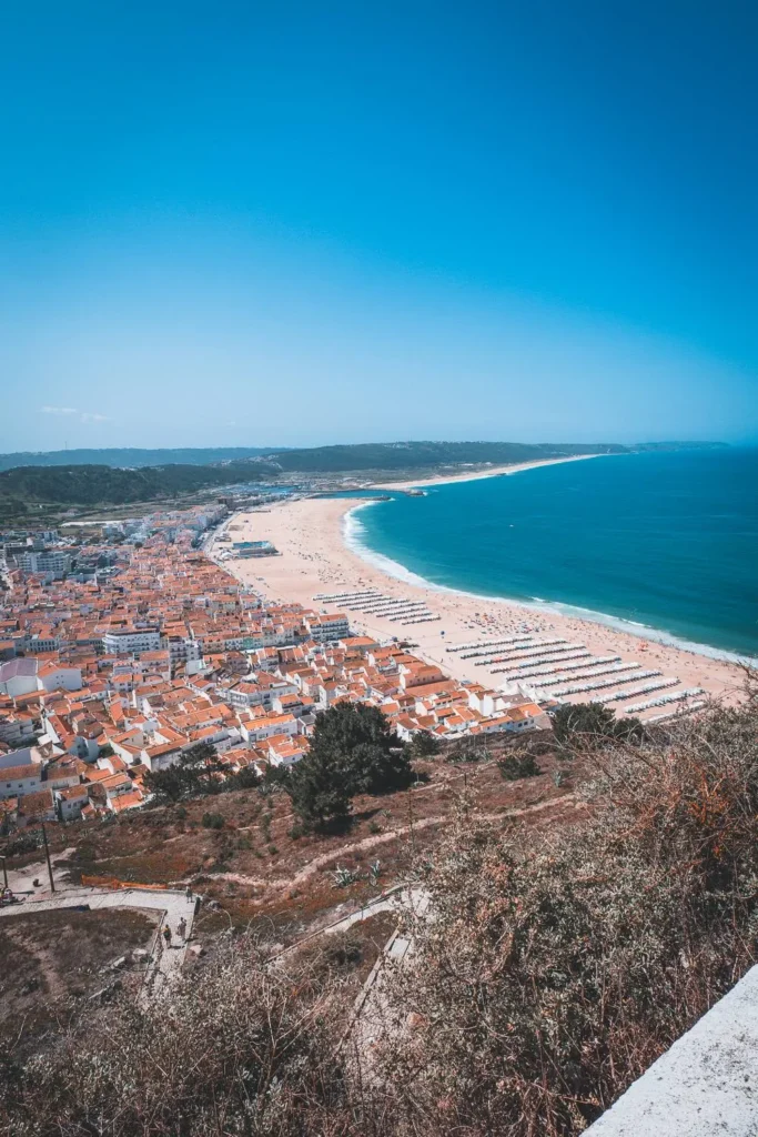 Panoramic view of Nazaré beach and the red rooftops of the village, with the Atlantic Ocean in the background on a clear summer day.