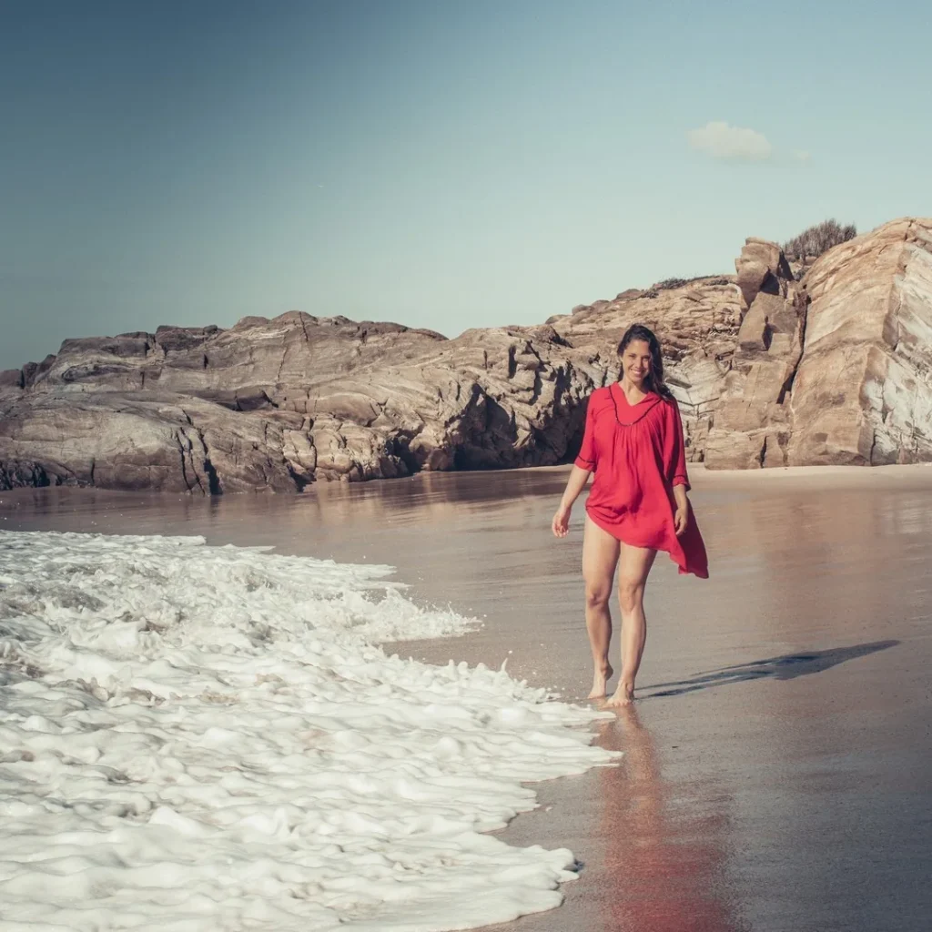 Caroline walks along the water's edge on Oliveirinha beach near Porto Covo, with rocks in the background under a clear sky in March 2022.