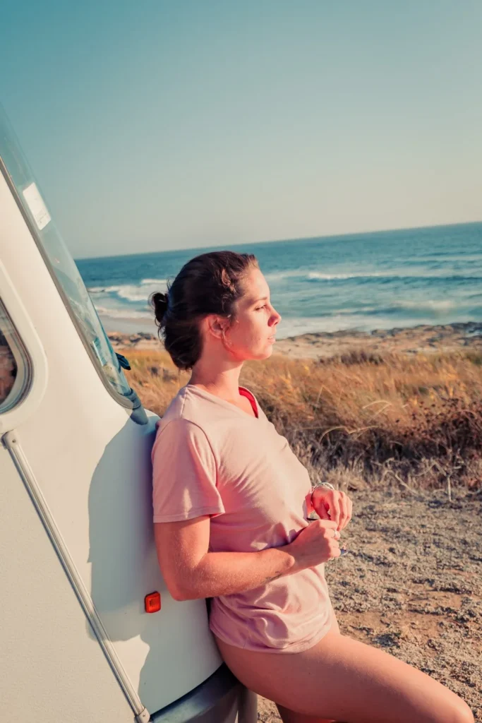 Caroline leaning against a van facing the ocean on Praia de Oliveirinha, near Porto Covo, under the summer light of Alentejo.