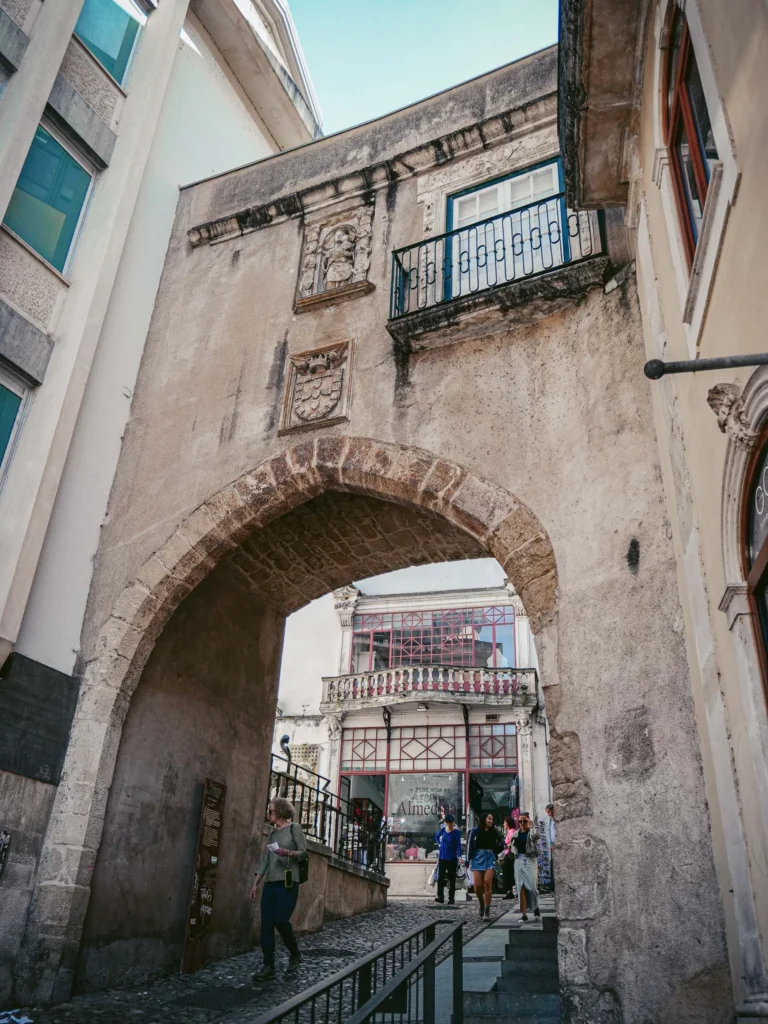 Medieval stone door in a street of the historic center of Coimbra, Portugal, with passersby and old buildings around.