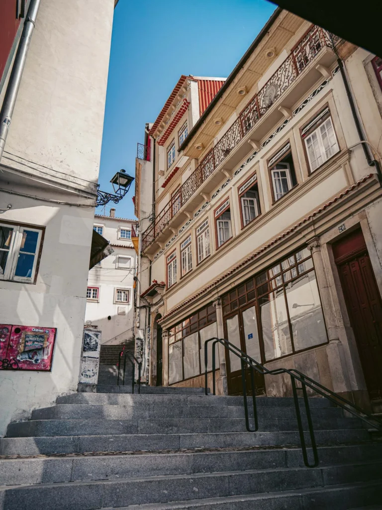Stone staircase in a typical alley of the historic center of Coimbra, with old buildings featuring decorated facades under a blue sky.