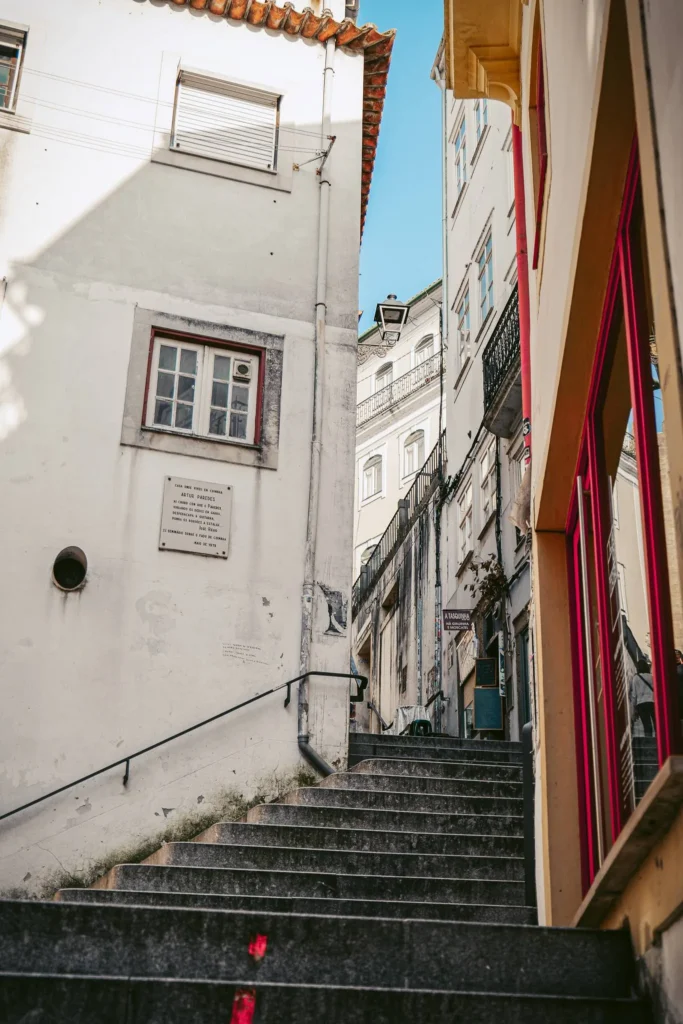 Narrow stone staircase lined with old buildings in an alley of the historic center of Coimbra on a sunny day.