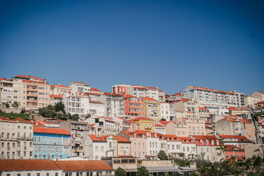 View of the colorful buildings with red roofs in Coimbra under a blue sky, typical of Portuguese architecture.
