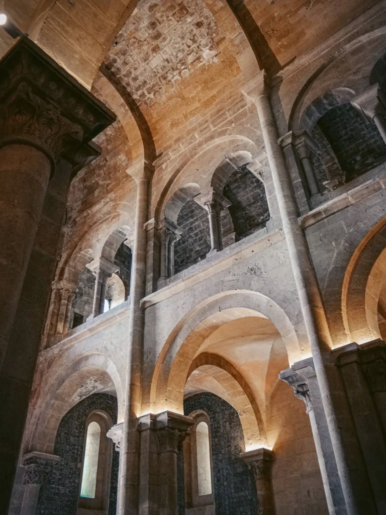 Vaulted interior of a Romanesque church in Coimbra, with stone arches and massive columns illuminated by natural light.