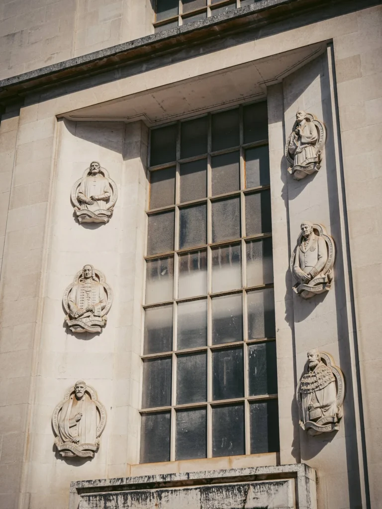 Facade of a stone building with a large window and six relief sculptures representing historical figures, probably in Coimbra, Portugal.