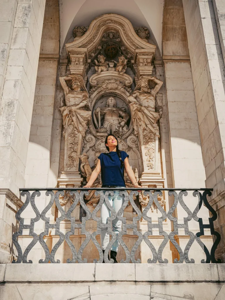 Caroline standing in front of a sculpted baroque facade in Coimbra, Portugal, under a stone arch.