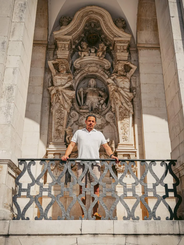 Xavier standing on a balcony in front of a sculpted stone facade in Coimbra, under sunny light.