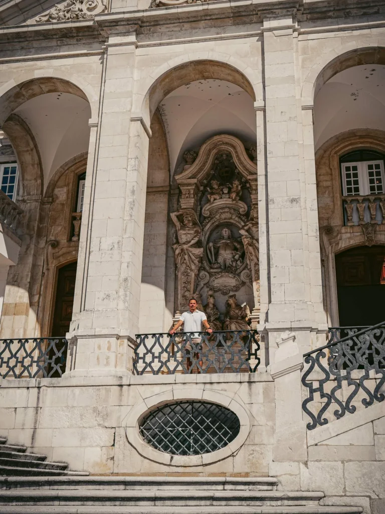 Xavier in front of a monumental stone façade in Coimbra, Portugal, with baroque sculptures and imposing arches.