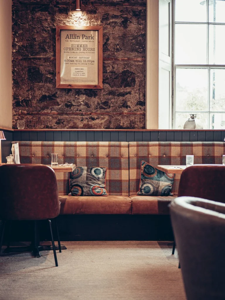 Bench corner of the Allan Park Hotel restaurant in Stirling, warm atmosphere with exposed stone wall and patterned cushions, natural light coming from the large window.