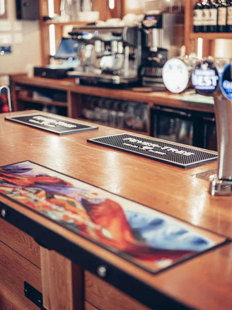 Wooden counter of the bar at the Allan Park Hotel in Stirling, with beer taps, coffee machine, and colorful decor, calm atmosphere with no visible customers.