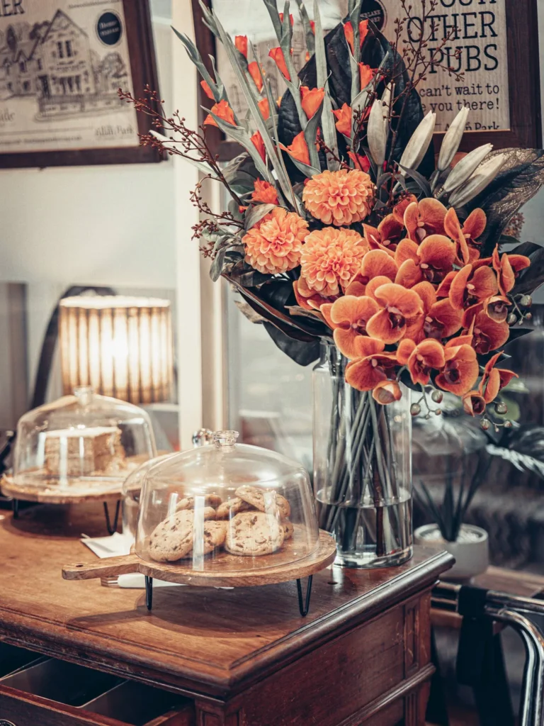 A platter of cookies under a glass dome and a large bouquet of orange flowers on a wooden table inside the Allan Park Hotel in Stirling, Scotland.