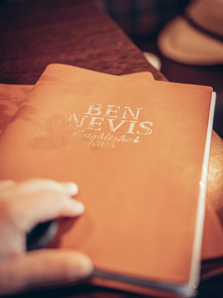 Leather menu from the Ben Nevis Bar placed on a wooden table in the Scottish Highlands, warm atmosphere.