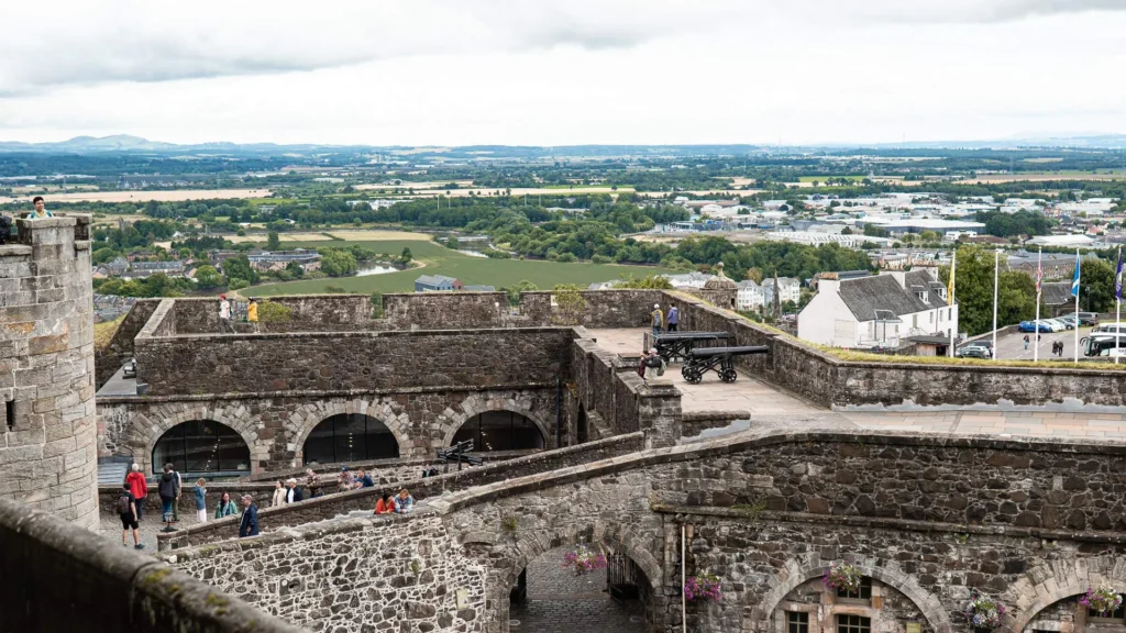 The ramparts and inner courtyard of Stirling Castle, with the Scottish countryside beyond under a cloudy sky.