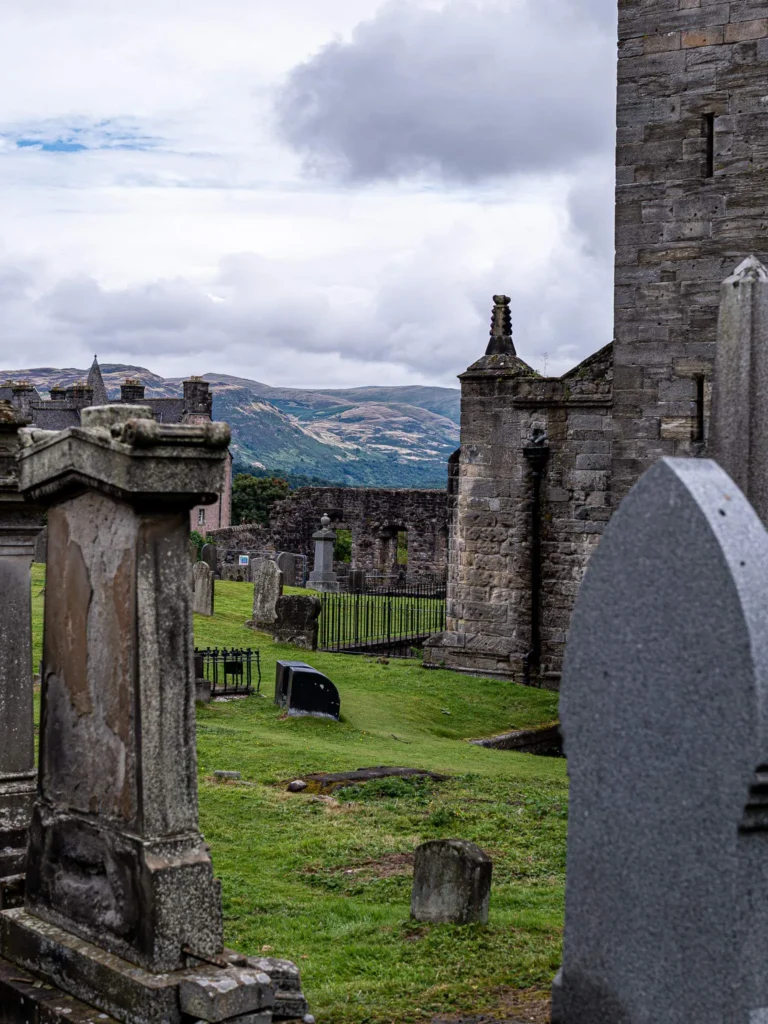 Kirkyard at the back of the Church of the Holy Rude, in Stirling: ancient gravestones overgrown with grass and a view of the surrounding countryside.