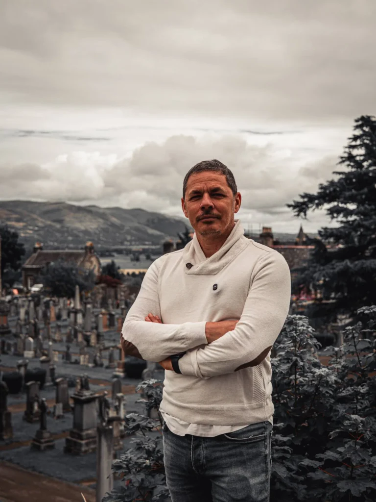 Xavier in front of the kirkyard of the Church of the Holy Rude, in Stirling, with a panorama of the countryside under a cloudy sky.