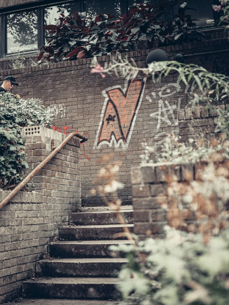 Xavier climbing a brick staircase lined with greenery, a colourful graffiti on the wall, in Glasgow.
