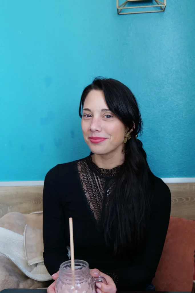 Caroline sitting in a restaurant in Lagos, Algarve, holding a smoothie in front of a blue wall.