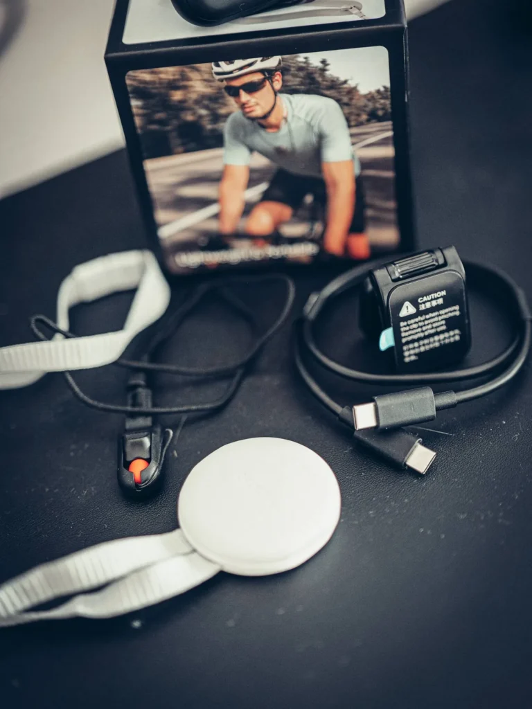 Primo piano degli accessori della Insta360 GO Ultra: clip con pulsante di sgancio arancione, supporto magnetico rotondo e cavo USB-C doppio.