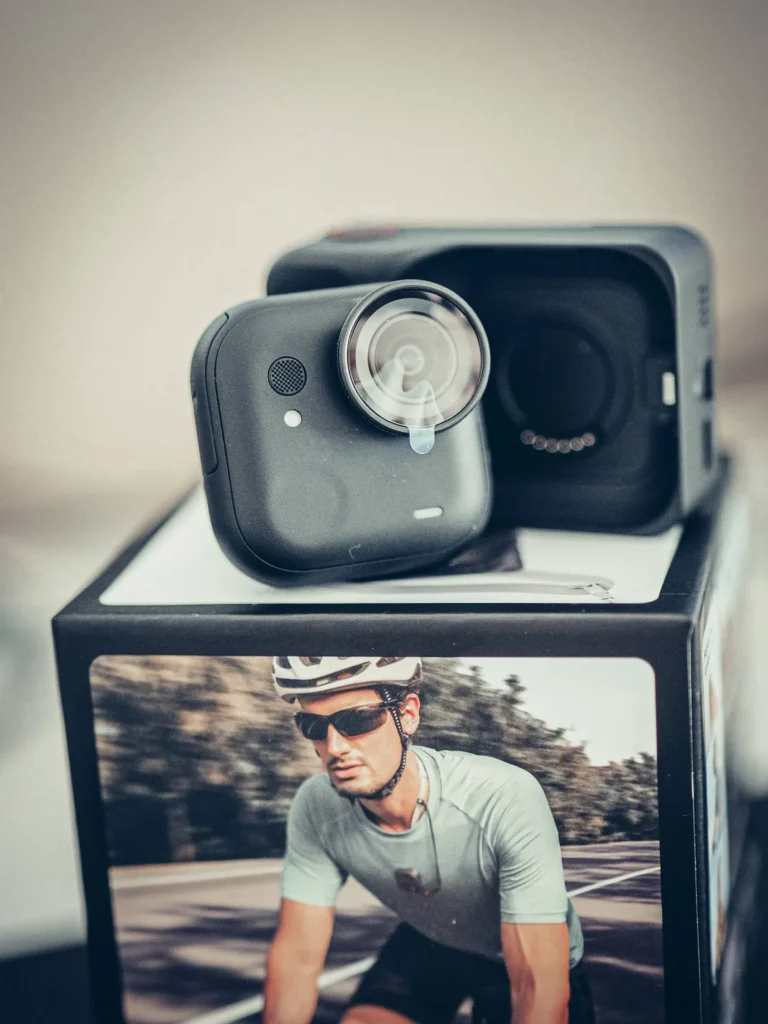 Il modulo fotocamera della Insta360 GO Ultra davanti al suo Action Pod, con l'alloggiamento magnetico del corpo ben visibile.