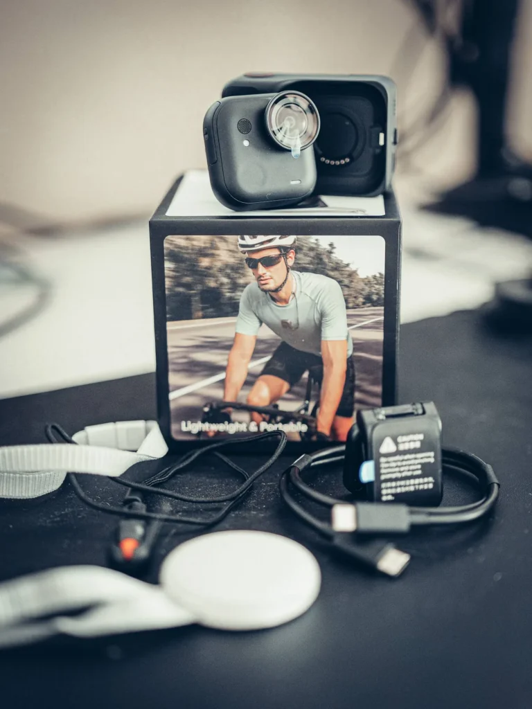 Il contenuto completo della scatola della Insta360 GO Ultra: la fotocamera sull'Action Pod, il laccetto, la clip magnetica, il supporto e il cavo USB-C disposti.