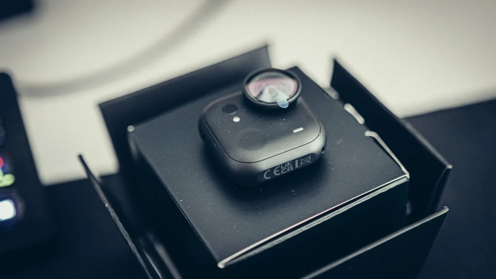 Il modulo fotocamera della Insta360 GO Ultra, nero opaco, appoggiato nel suo alloggiamento all'apertura della scatola, con la pellicola protettiva ancora sull'obiettivo.