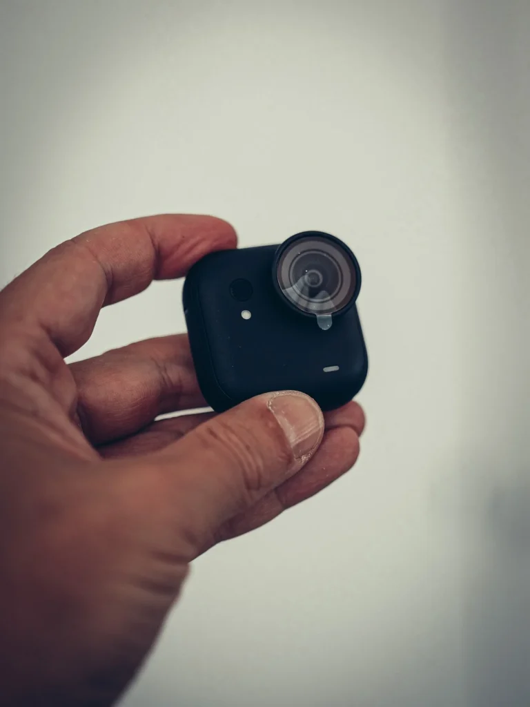 Il modulo fotocamera della Insta360 GO Ultra tenuto in mano, lato anteriore con obiettivo e microfono, su sfondo chiaro.