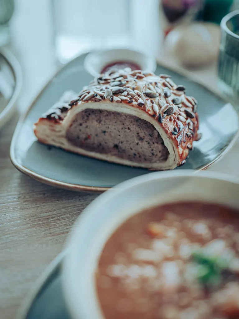 Seeded sausage roll and Ham Hock and Lentil Soup served together on a wooden table at the Linnhe Storehouse and Cafe at Portnacroish, Argyll.