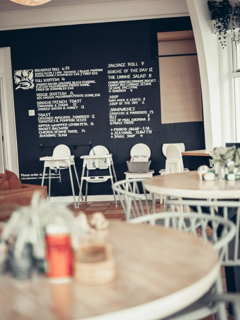 The large polygonal room at the Linnhe Storehouse and Cafe at Portnacroish, Argyll, with its wooden tables, tall stools and the day's menu chalked on a black wall.
