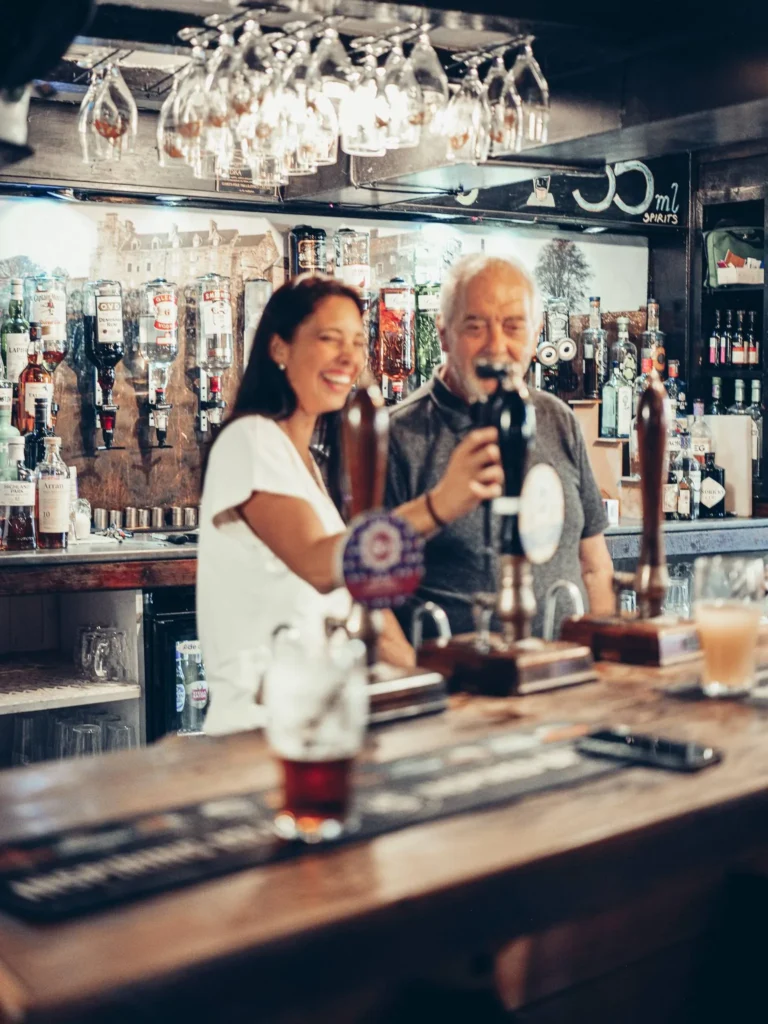 Caroline and Xavier at the counter of the Settle Inn, in Stirling, surrounded by bottles and glasses hanging above the bar.