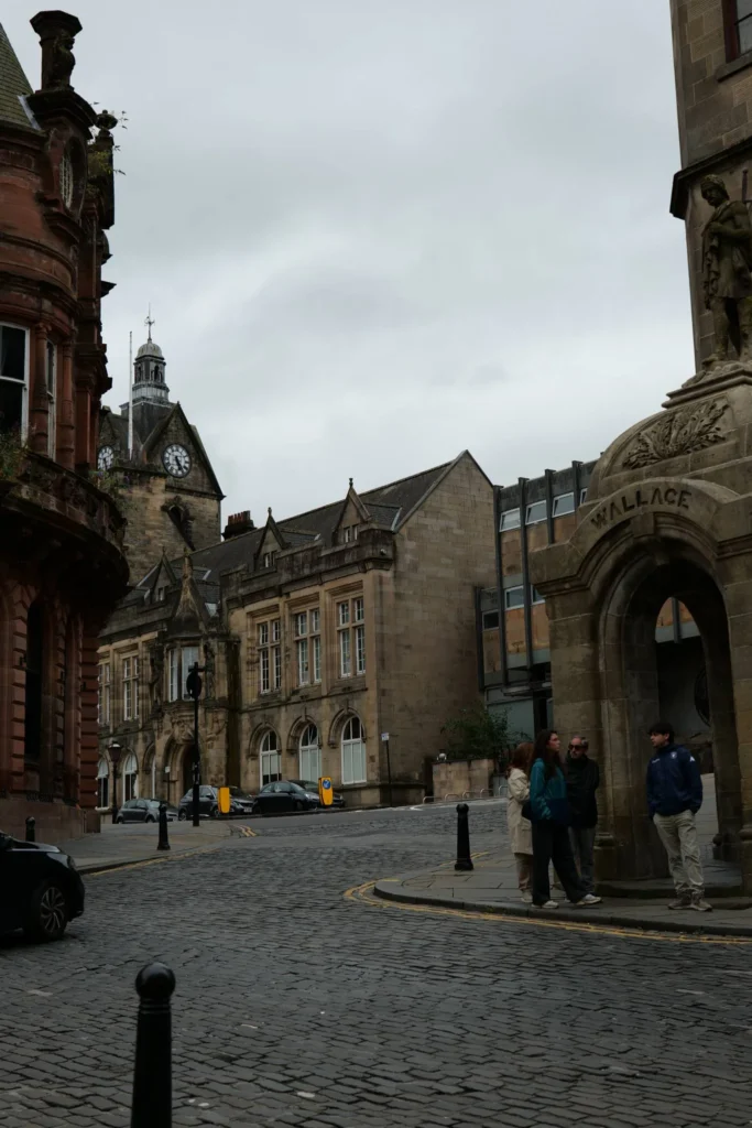 Caroline and Xavier are discussing on a cobbled street in the old town of Stirling, between the stone buildings, under a grey sky.