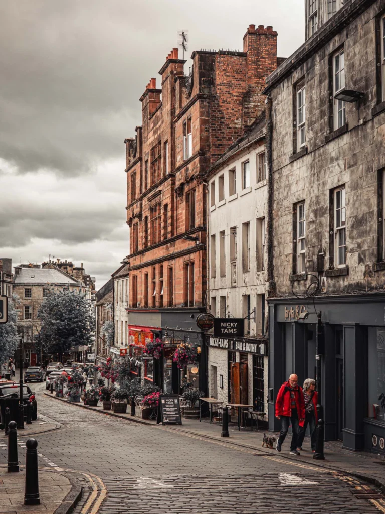 Caroline and Xavier walk up a steep street in the old town of Stirling, between the stone facades, pub signs, and antique street lamps.