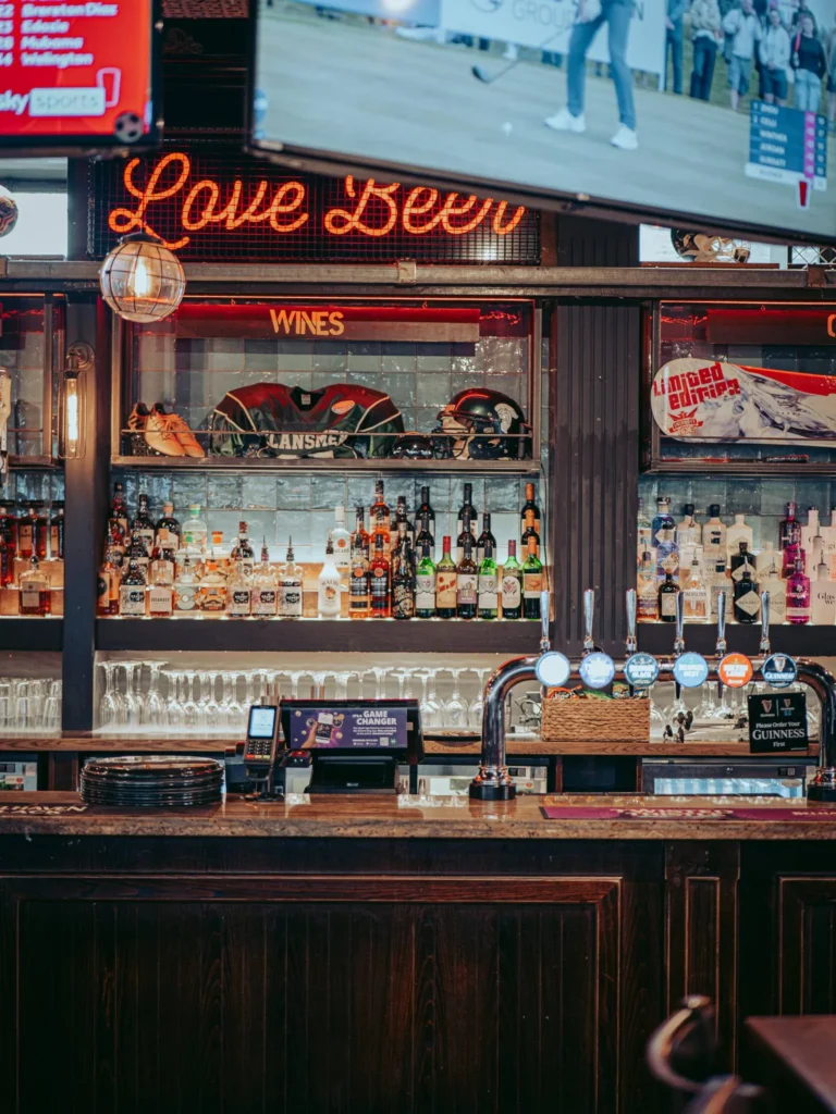 Counter of a pub in Stirling: lined bottles, beer taps, and sports decor under a bright sign "Love Beer". Unidentified establishment.