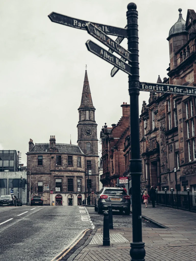 Steep street of the old town of Stirling: stone and sandstone buildings, black lamppost with a four-faced glass lantern, bell tower in the background.