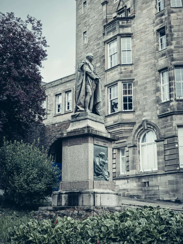 Stone statue in front of a large sandstone building with mullioned windows, in the old town of Stirling.