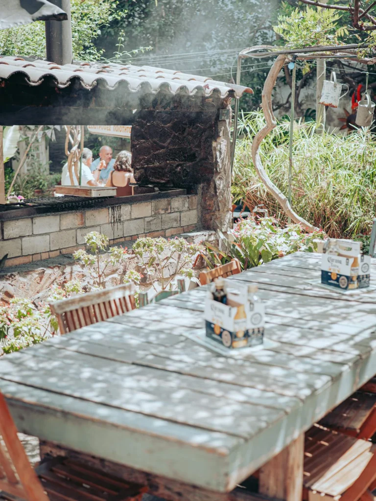 Wooden table in the garden of The Garden Bar and Grill in Lagos, facing the covered barbecue and the kitchen set up in a sort of open garage.