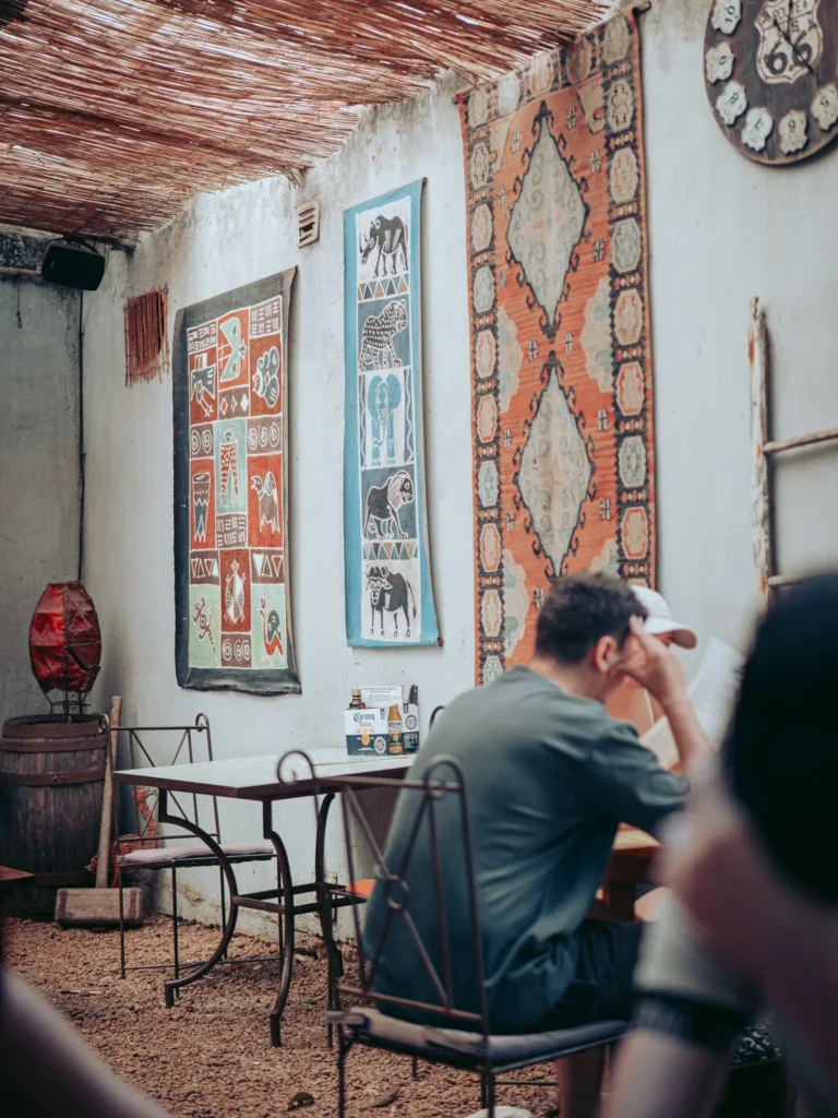 Semi-covered area of The Garden Bar and Grill in Lagos, surrounded by three walls, topped with a thatched roof and decorated with wall carpets.