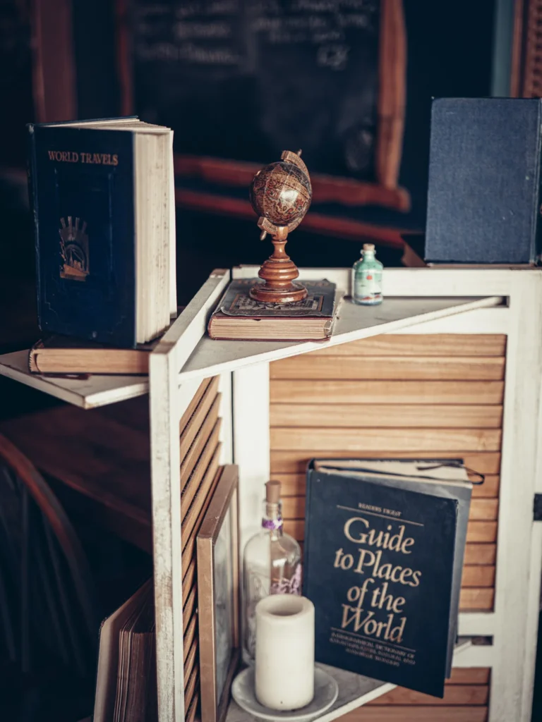 Restaurant decor with a white shelf displaying travel books, a small globe, a candle, and a bottle, in a cozy atmosphere in Fort William in the Scottish Highlands in August 2026.