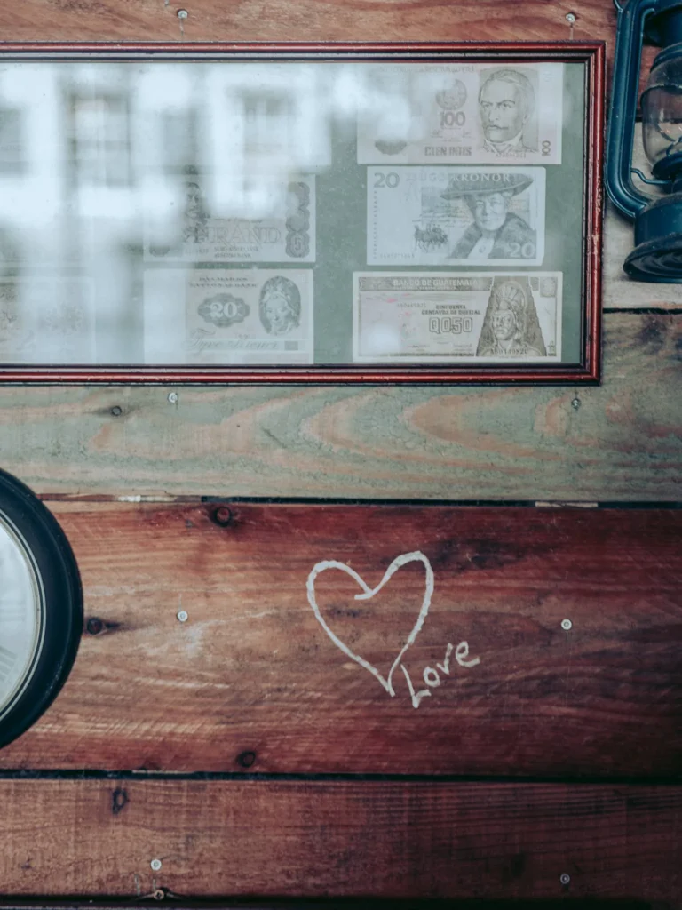 Frame with foreign banknotes displayed on a wooden wall, featuring a heart drawing and the word 'love' written in chalk. Rustic atmosphere in a restaurant in the Scottish Highlands.