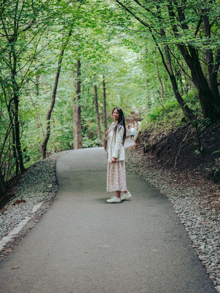 Caroline walks along a forest path surrounded by lush trees near the Wallace Monument in Stirling, Scotland, in August 2026.
