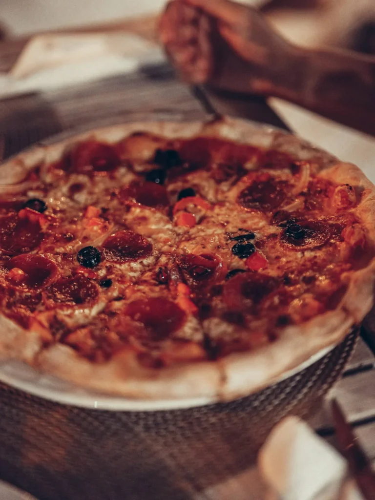 Pepperoni and olive topped pizza served on a restaurant table, warm atmosphere typical of a pizzeria in Tavira, Algarve.