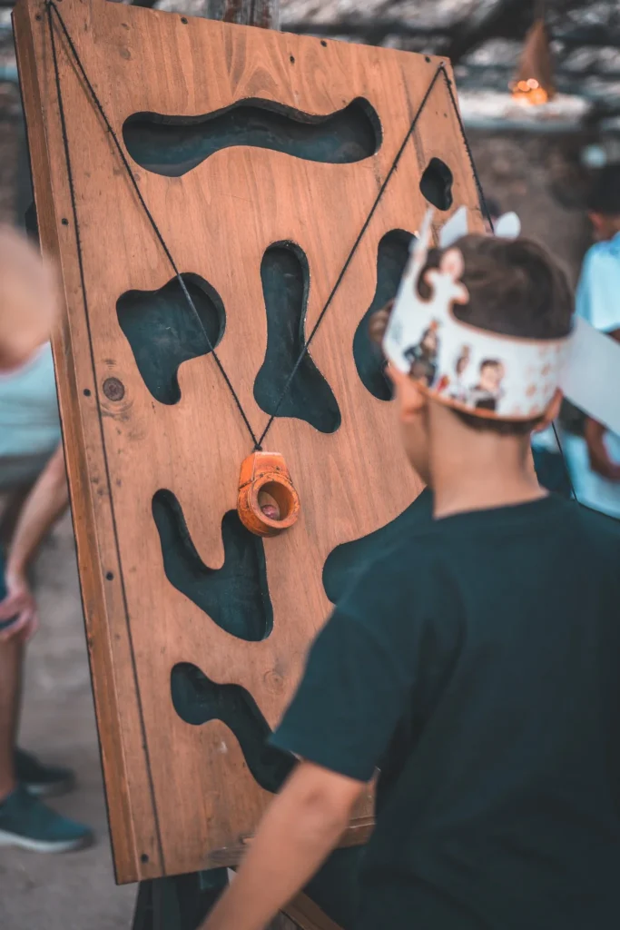 Wooden maze game being manipulated by a child wearing a paper crown during an outdoor activity at the medieval festival of Castro Marim.