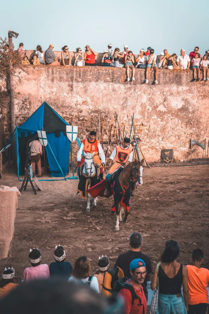 Knights' tournament in armour at the Castro Marim medieval festival, spectators seated on the ramparts and tents decorated with coats of arms.