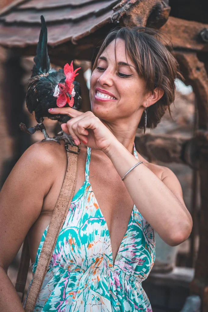 Caroline smiles while holding a rooster on her arm, dressed in a floral dress at the medieval festival of Castro Marim in the Algarve.