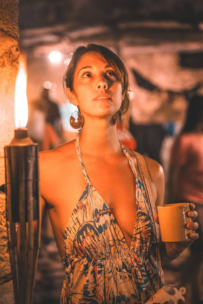 Caroline in a flowered dress holding a cup, lit by a torch during a medieval evening in Castro Marim.