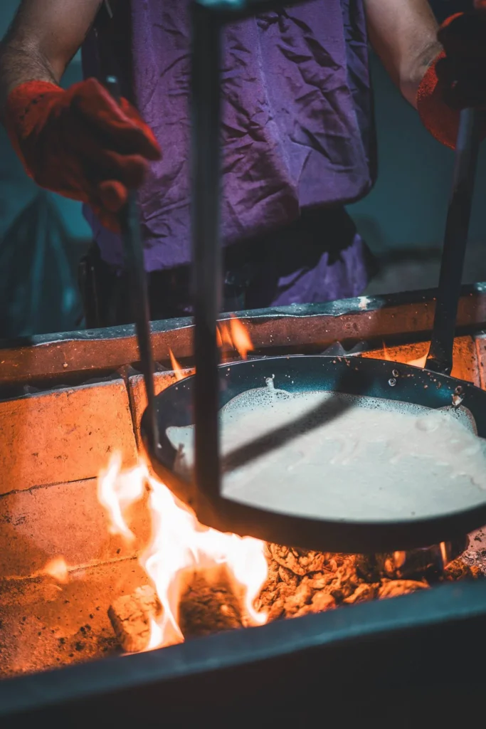 A craftsman in medieval attire handles a pan suspended over a wood fire, likely during a cooking demonstration at the medieval festival of Castro Marim in the Algarve.