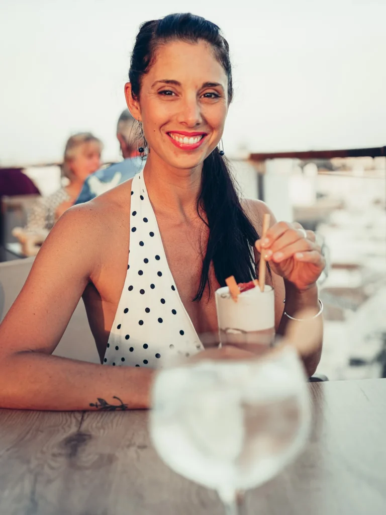 Caroline seated on the terrace of the Nomad, the rooftop of the Maria Nova Lounge Hotel in Tavira, smiling in a polka dot dress, her Rooftop Gin in hand at the start of the evening.