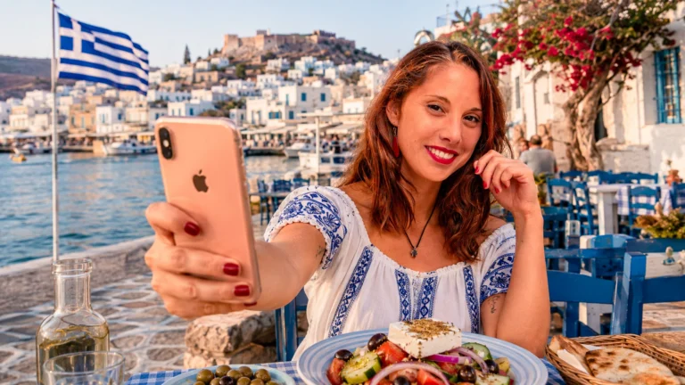 Caroline si fa un selfie con lo smartphone al porto di Naxos, in Grecia, con vista sulla città vecchia.